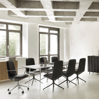 Modern office space featuring black chairs, white walls, and exposed concrete ceilings, with a minimalist design.