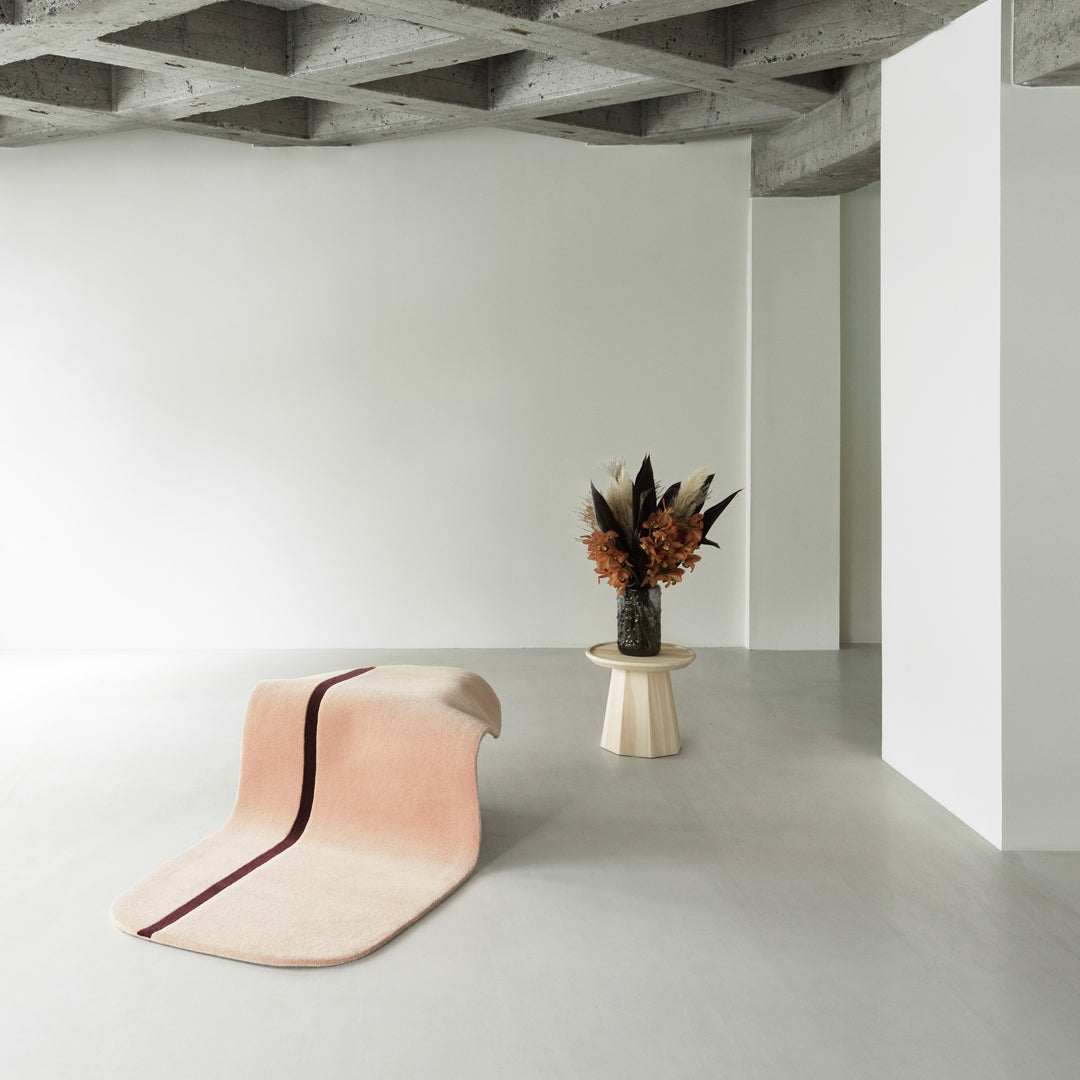 Soft pink rug with a contrasting burgundy stripe, against a minimalist neutral backdrop.