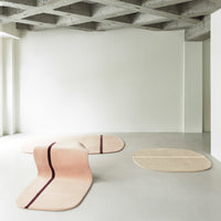 Soft pink and beige area rugs with geometric patterns and contrasting stripes, set against a minimalist background.