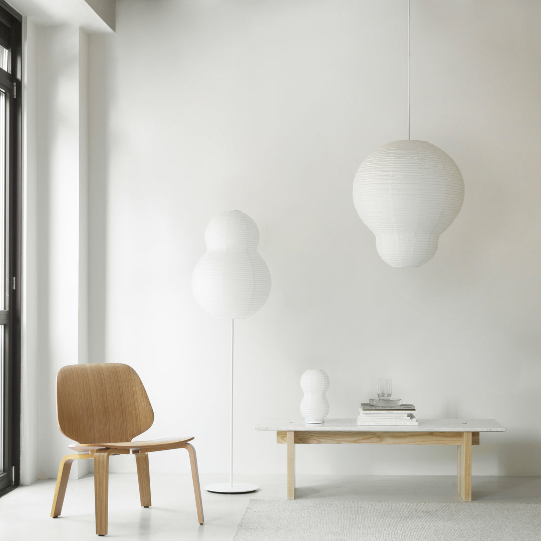 White pendant lights and a modern wooden chair in a minimalist living room with neutral tones and soft shapes.