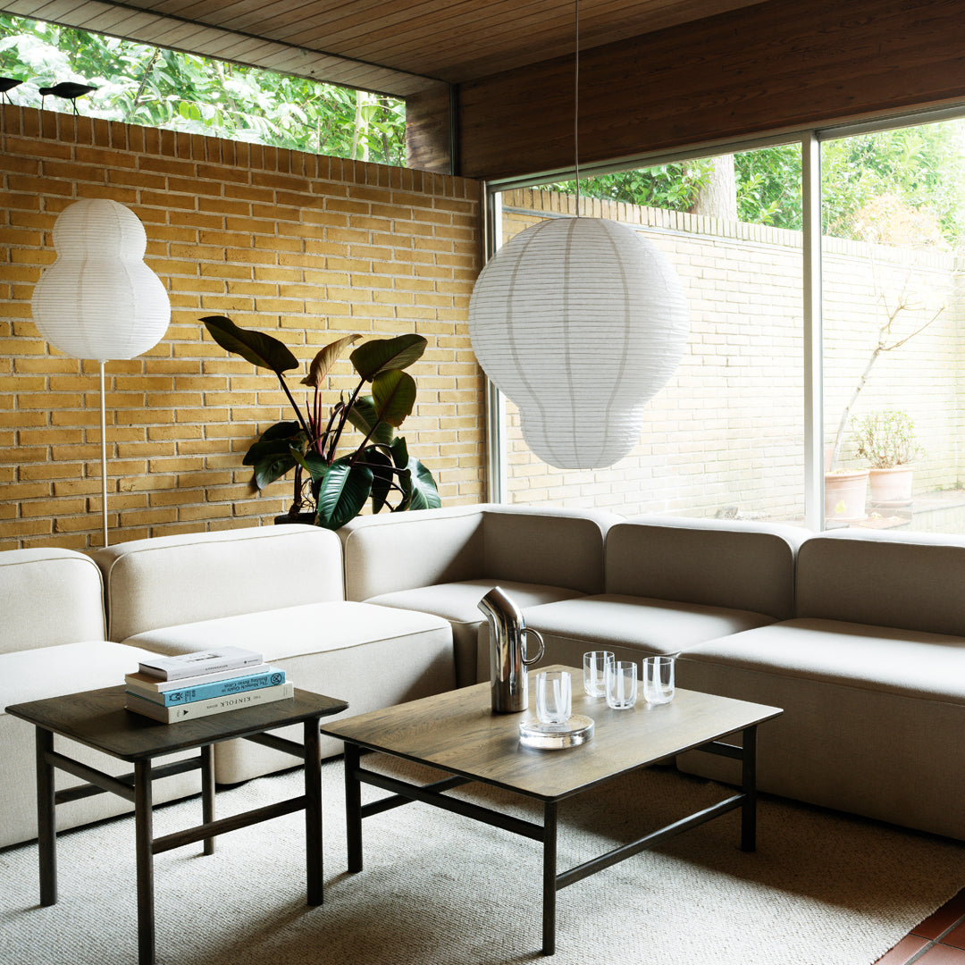 Neutral beige sectional sofa, minimalist black accent tables, and soft white lighting in a serene indoor setting.