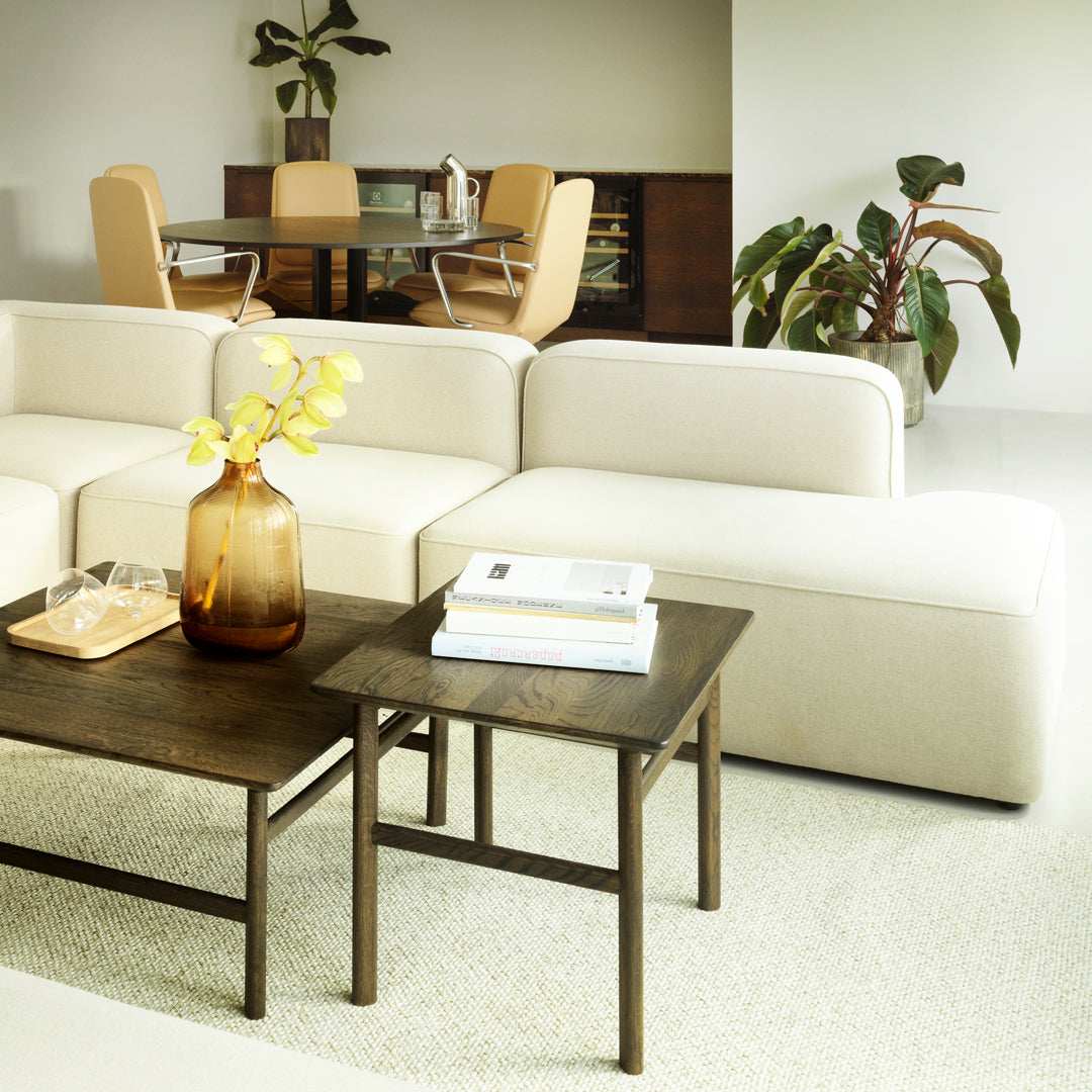 Beige modular sofa with a dark wood table, yellow accents, and a neutral patterned rug in a modern living room setting.