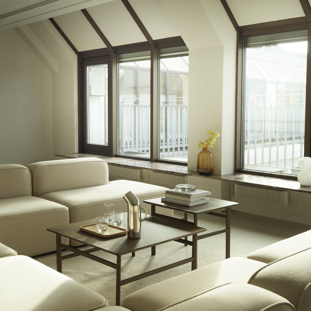 Neutral beige sectional sofa with light gray and brown accents, set against a bright, airy room with large windows.