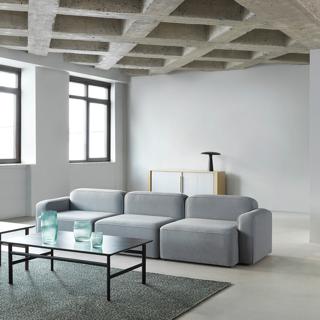 Light gray sectional sofa with smooth fabric, accented by a textured dark green rug. Modern and minimalistic design.