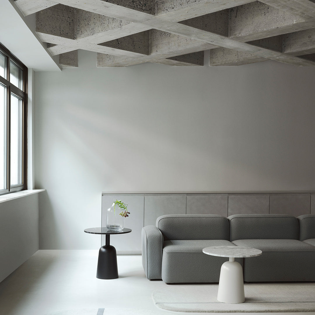 Grey textured sofa, minimalist black and white tables, and soft neutral walls create a modern, elegant living space.