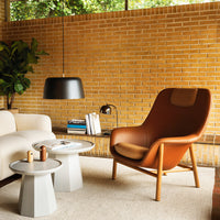 Stylish brown leather chair with light gray side tables, contrasting against a textured yellow brick wall.
