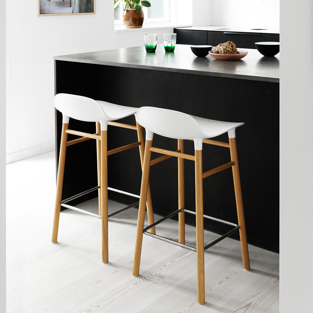 White bar stools with natural wood legs, set against a sleek black kitchen island in a modern, minimalist setting.