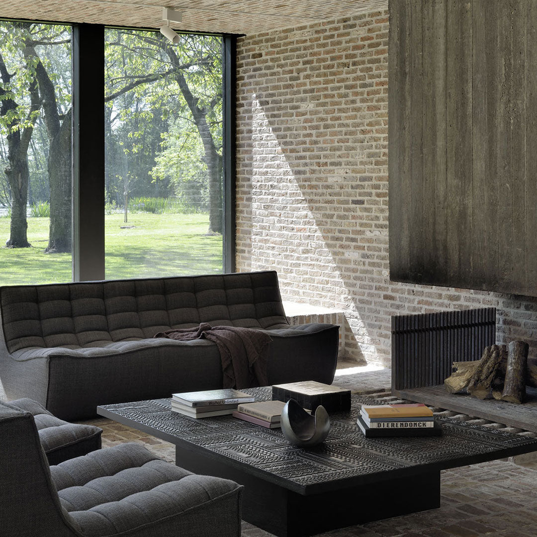 Modern living room with gray furniture, textured brick wall, and natural light highlighting clean lines and dark wood accents.