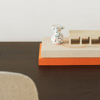 Colorful patterned decor on stacked books with orange and natural beige tones, set on a dark wooden surface.