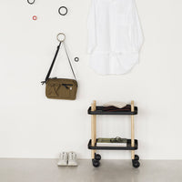 White blouse, olive green bag, black and natural wood cart, and black/red circular wall decor against a minimalist backdrop.
