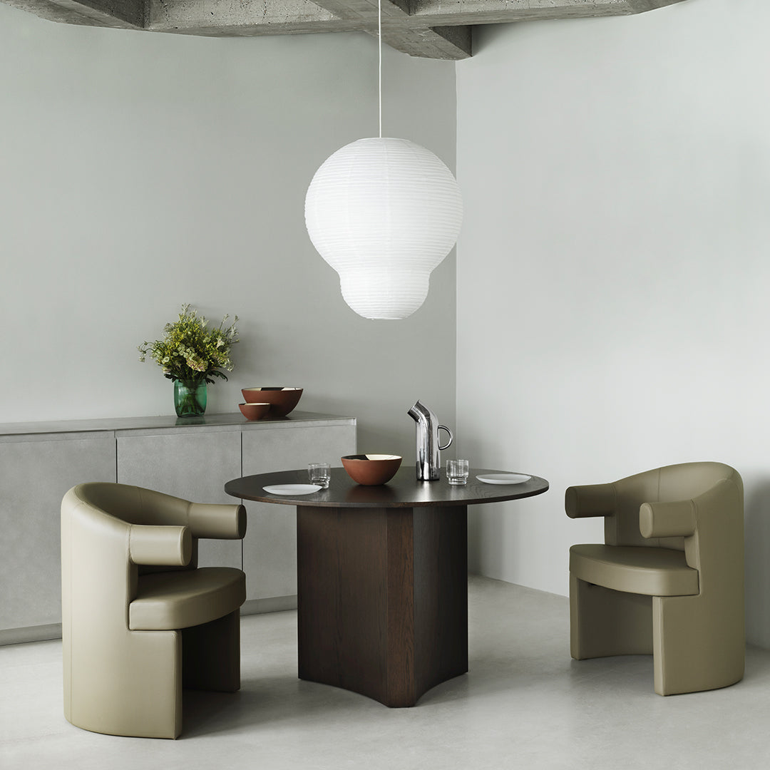 Neutral-toned dining set with curved chairs and a round table, highlighted by a large white pendant light.