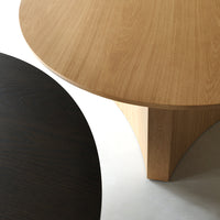 "Two modern round tabletops: one in light oak wood, the other in deep black, featuring smooth textures and clean lines."