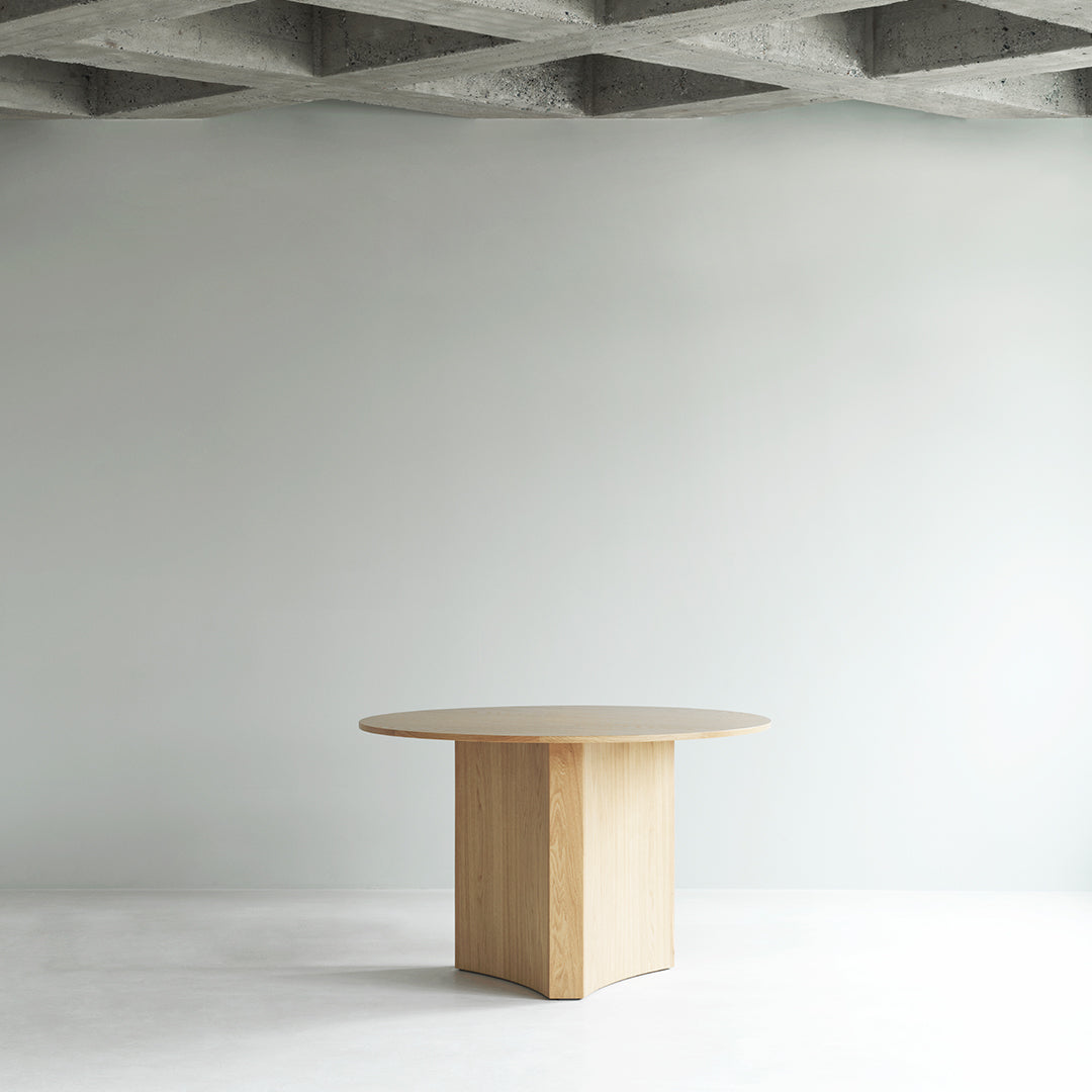Light wood round table with a smooth surface and minimalist design, set against a neutral gray background.