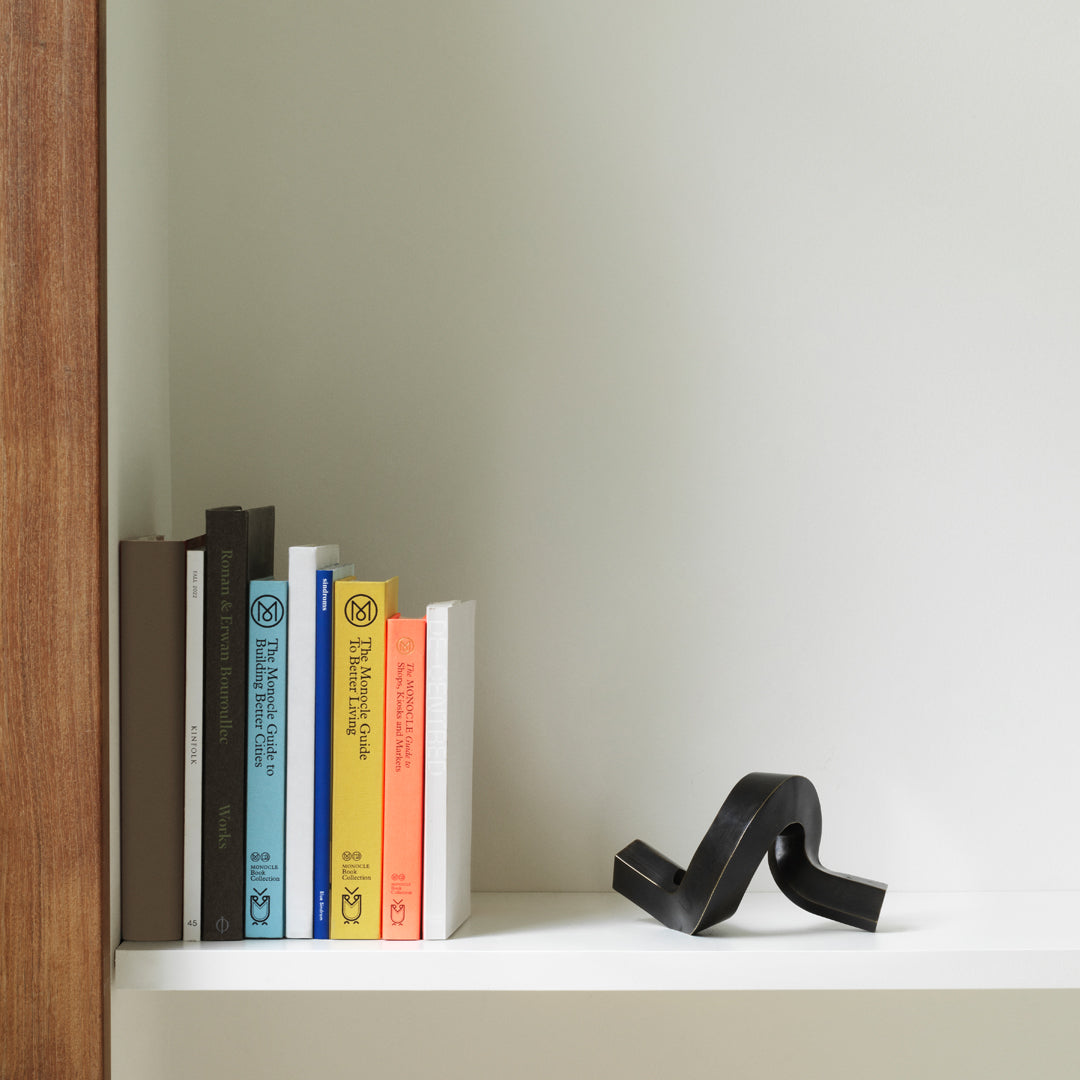 "Colorful books in pastel shades with a sleek black decorative piece on a minimalist white shelf."