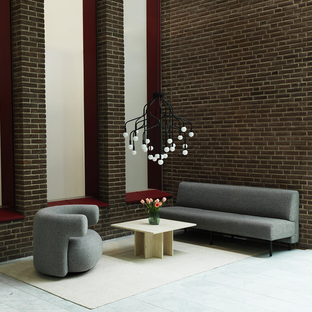Gray and cream upholstered sofa, curved gray armchair, and a minimalist wooden table against a brick wall backdrop.