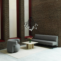 Gray upholstered furniture with minimalist design, featuring smooth curves and clean lines against a textured brick backdrop.