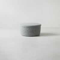 Soft gray round storage container with a minimalistic design and a textured felt pattern. Ideal for modern decor.