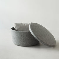 Gray felt decorative storage basket with a smooth rounded lid and a soft white cushion inside. Modern, minimalist design.
