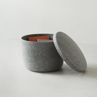 Gray felt storage basket with a round lid, featuring a vibrant orange interior. Minimalist design, perfect for home decor.