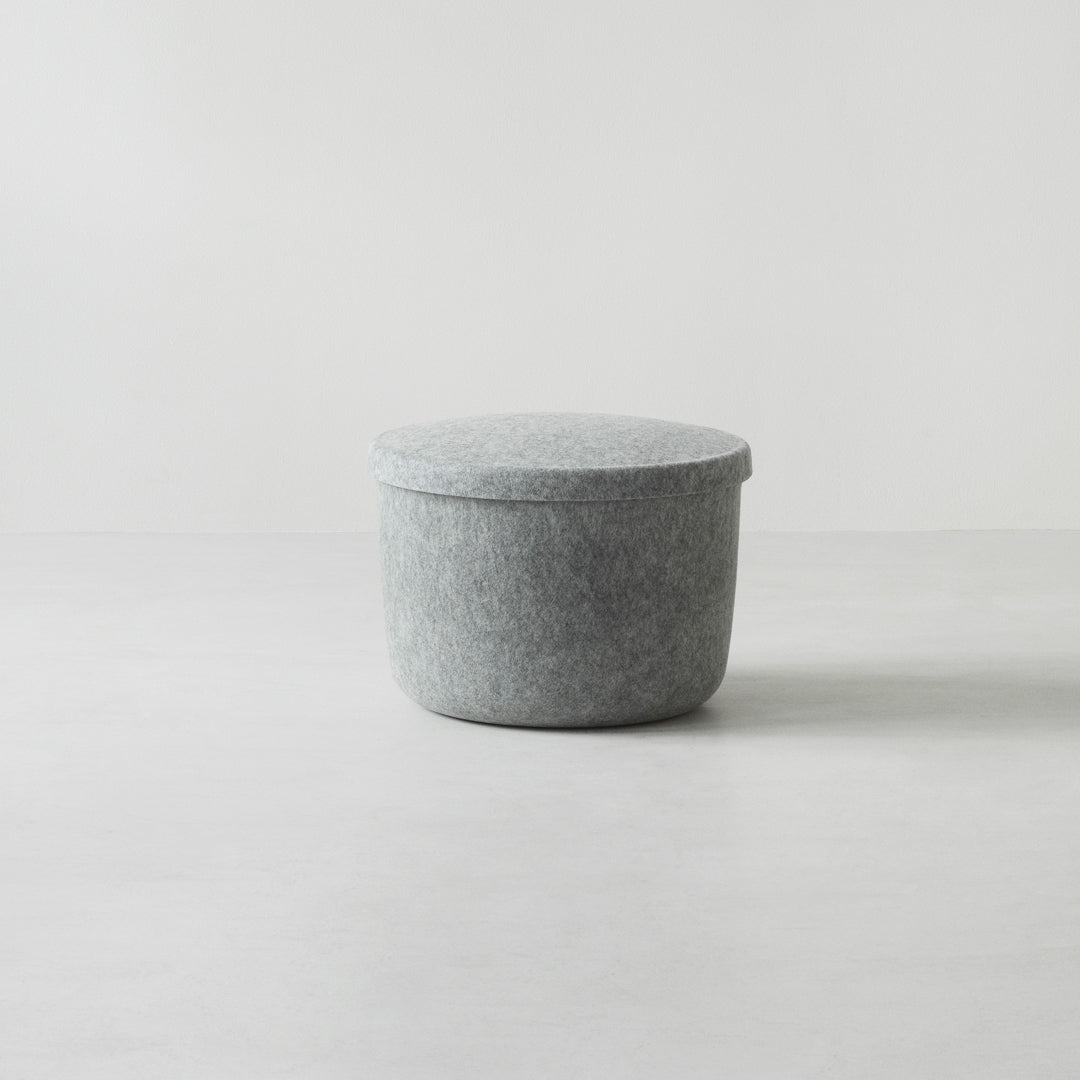 Gray felt storage ottoman with a smooth round top, perfect for modern decor. Minimalist design with a soft texture.