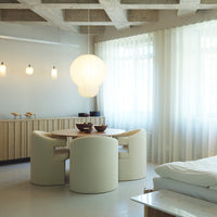 Modern dining room featuring neutral tones, soft textures, and round white furniture, illuminated by warm pendant lighting.
