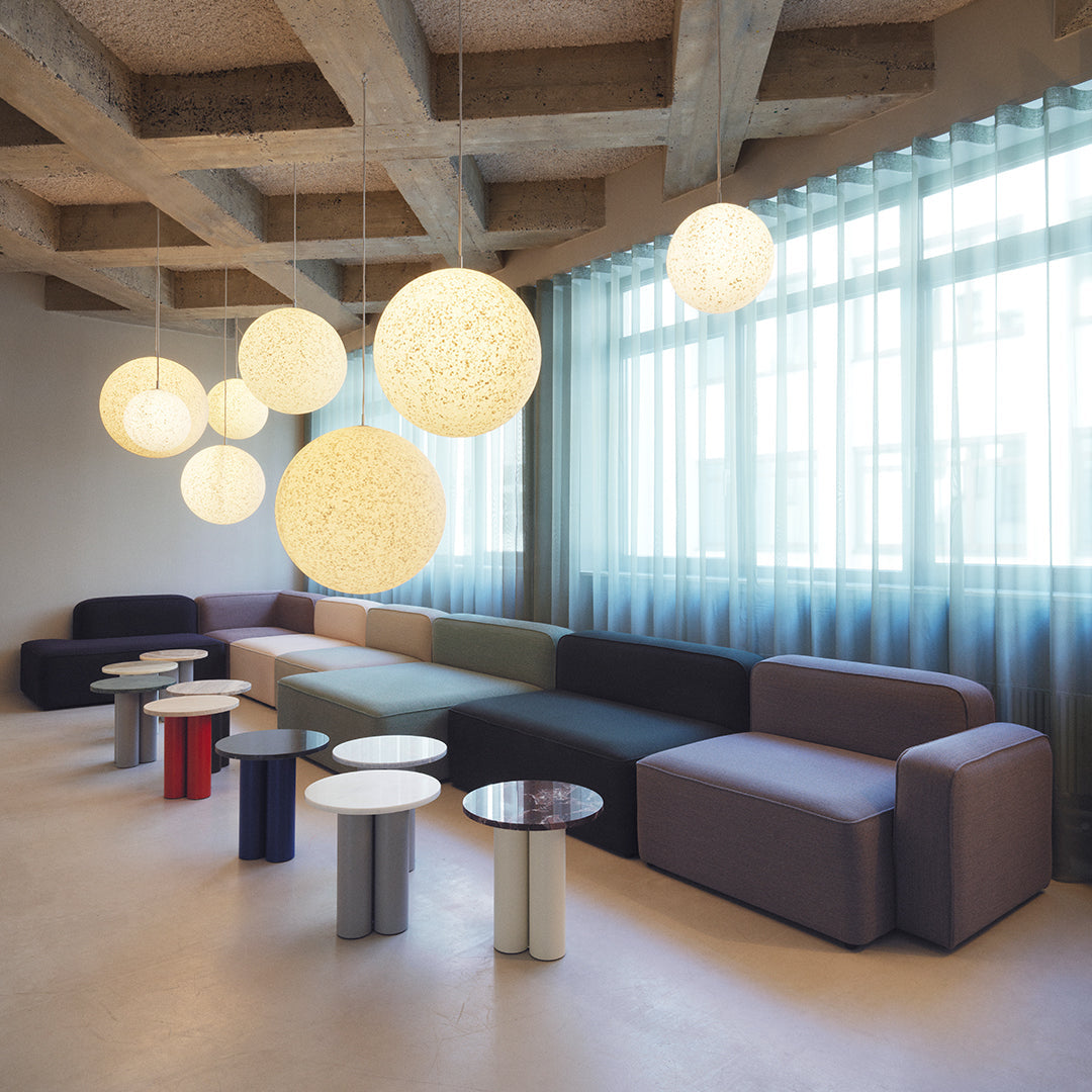 Modern lounge with gray, purple, and green sofas, and circular pendant lights, featuring white and translucent patterns.