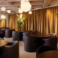Elegant gold curtains with a shimmering pattern, dark circular tables, and cozy gray seating in a modern setting.