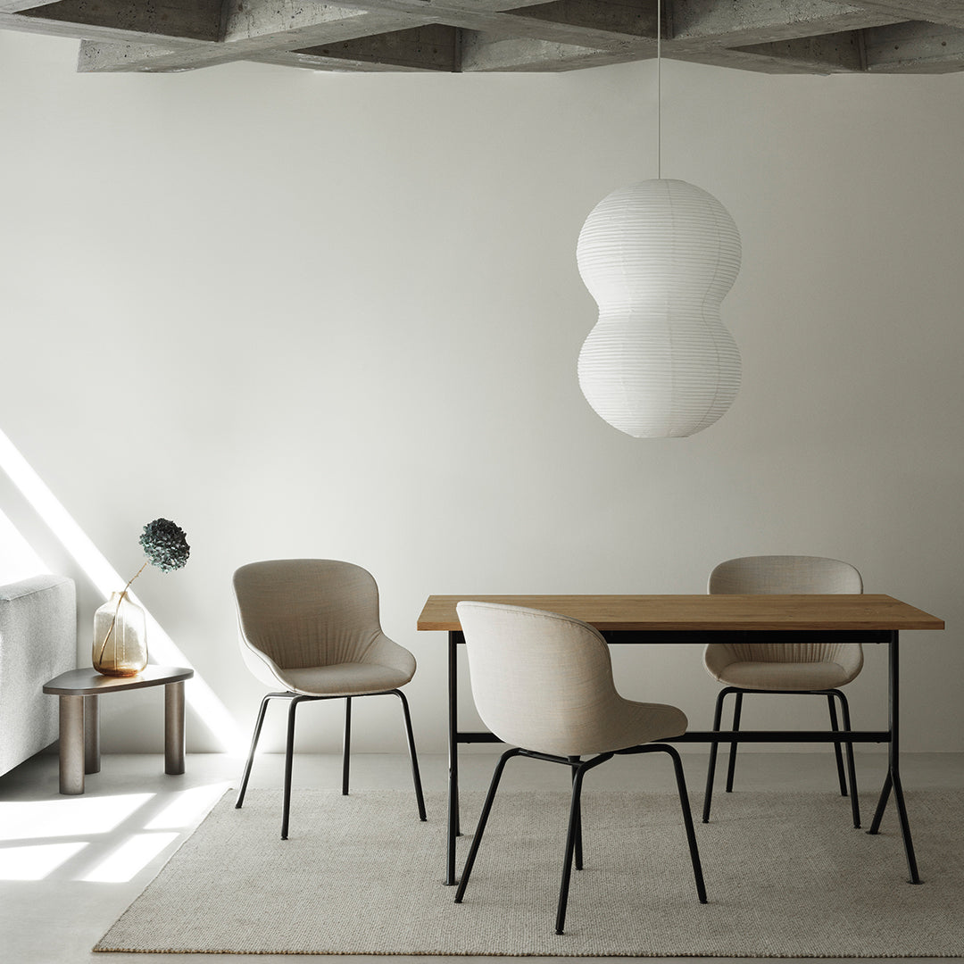 Neutral beige chairs and wooden table under soft, round pendant light, set against a minimalist, light-filled room.
