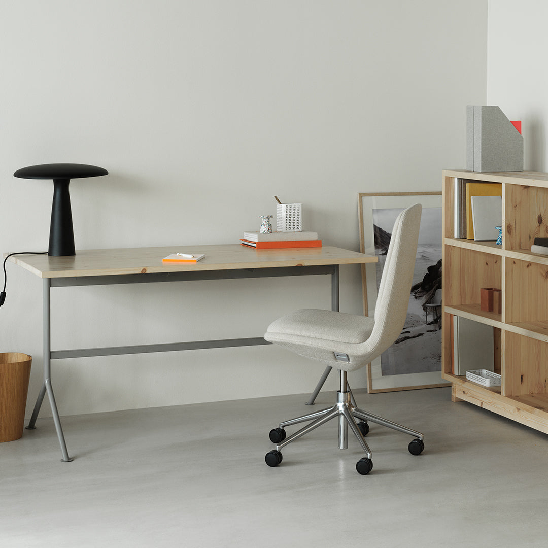 Modern desk with a light wood top, gray metal legs, and a white chair in a neutral-toned room. Orange accents. 