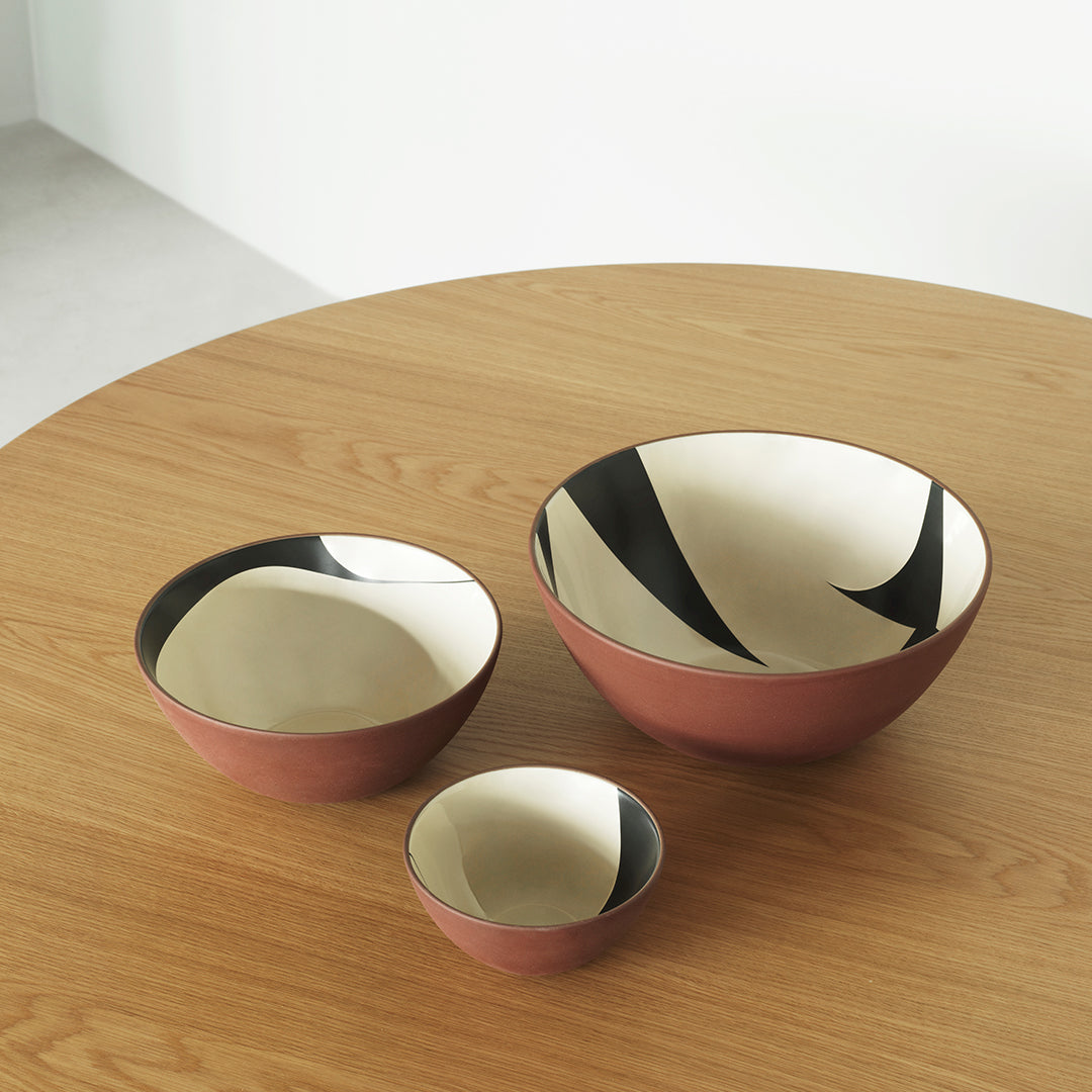 "Set of three ceramic bowls in warm terracotta and cream, featuring bold black and white abstract patterns."