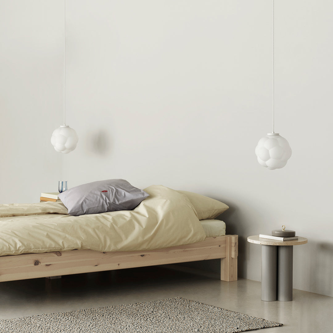 Soft yellow bedding with a gray pillow, complemented by white cloud-shaped pendant lights and a textured gray rug.