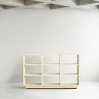 Light wood bookshelf with a minimalist design and open shelving, set against a smooth, neutral wall.