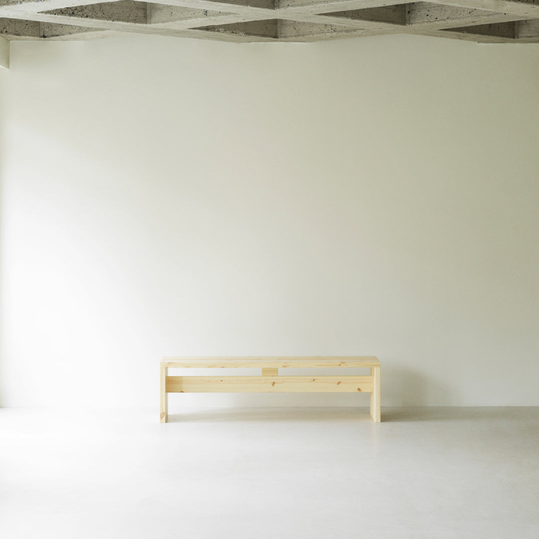 Light wooden bench with a natural finish against a minimalistic white wall and smooth gray floor.