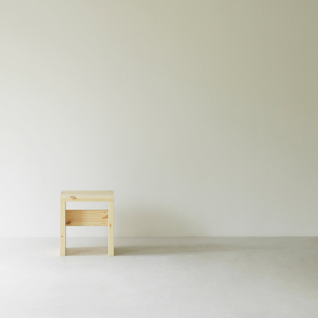 Light natural wood stool on a minimalist, neutral backdrop, showcasing a simple, modern design.