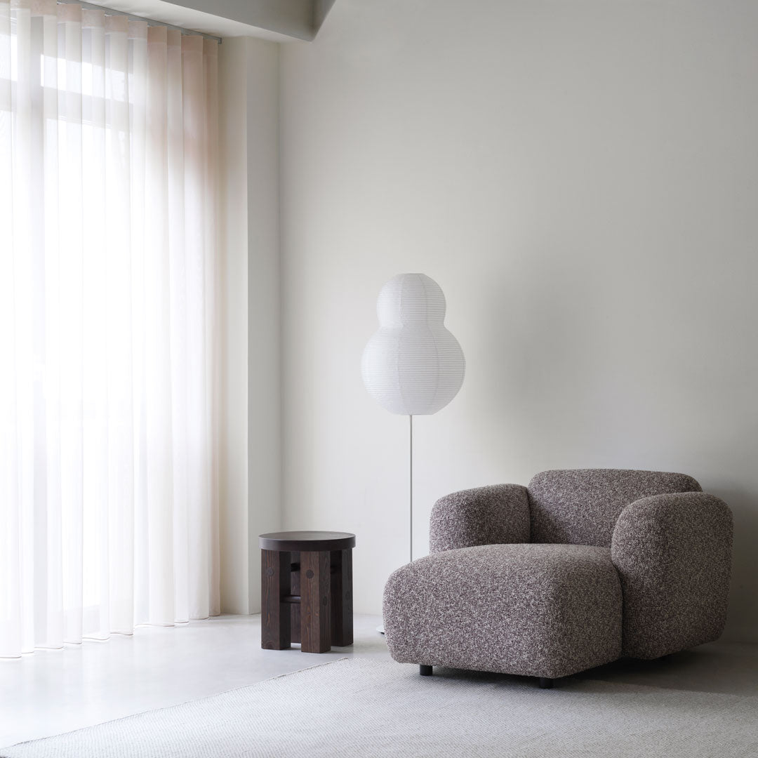 Cozy taupe upholstered armchair with a soft textured pattern, complemented by a minimalist white lamp and dark side table.