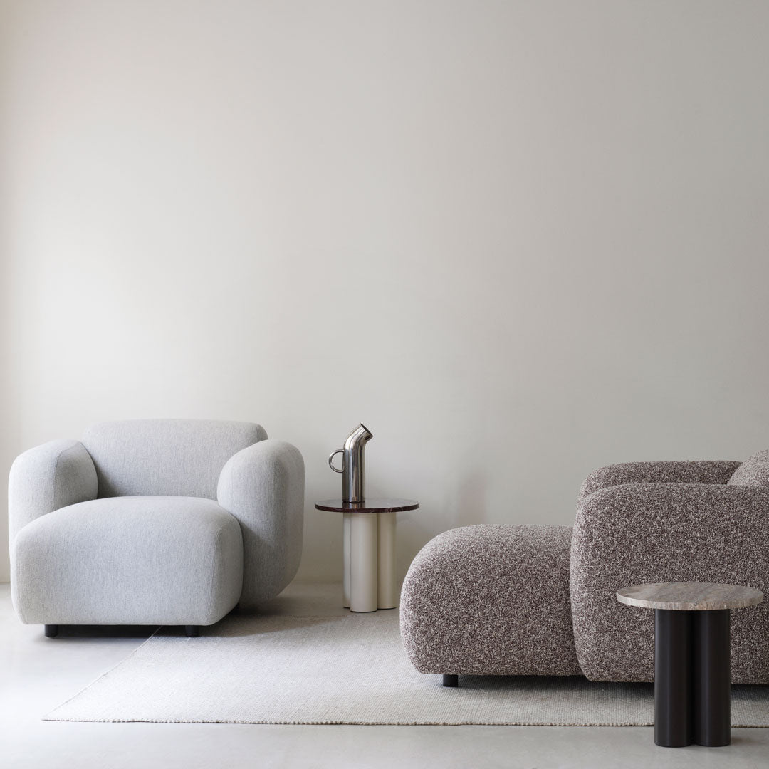 Soft gray and textured beige upholstery armchairs with sleek round tables in stylish neutral interior setting.