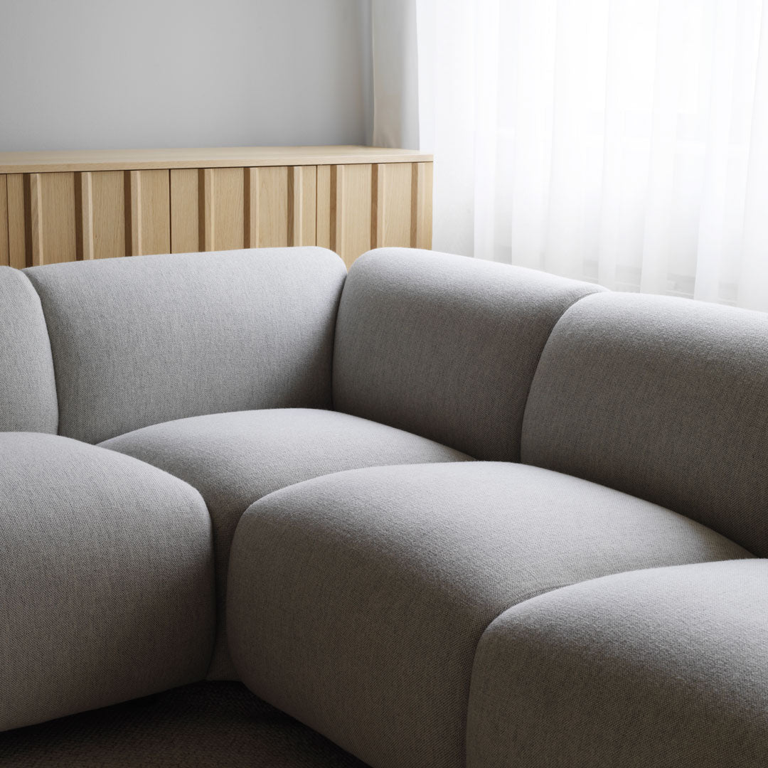 Gray modular sofa with smooth, minimalistic curves, complemented by a warm wooden backdrop.