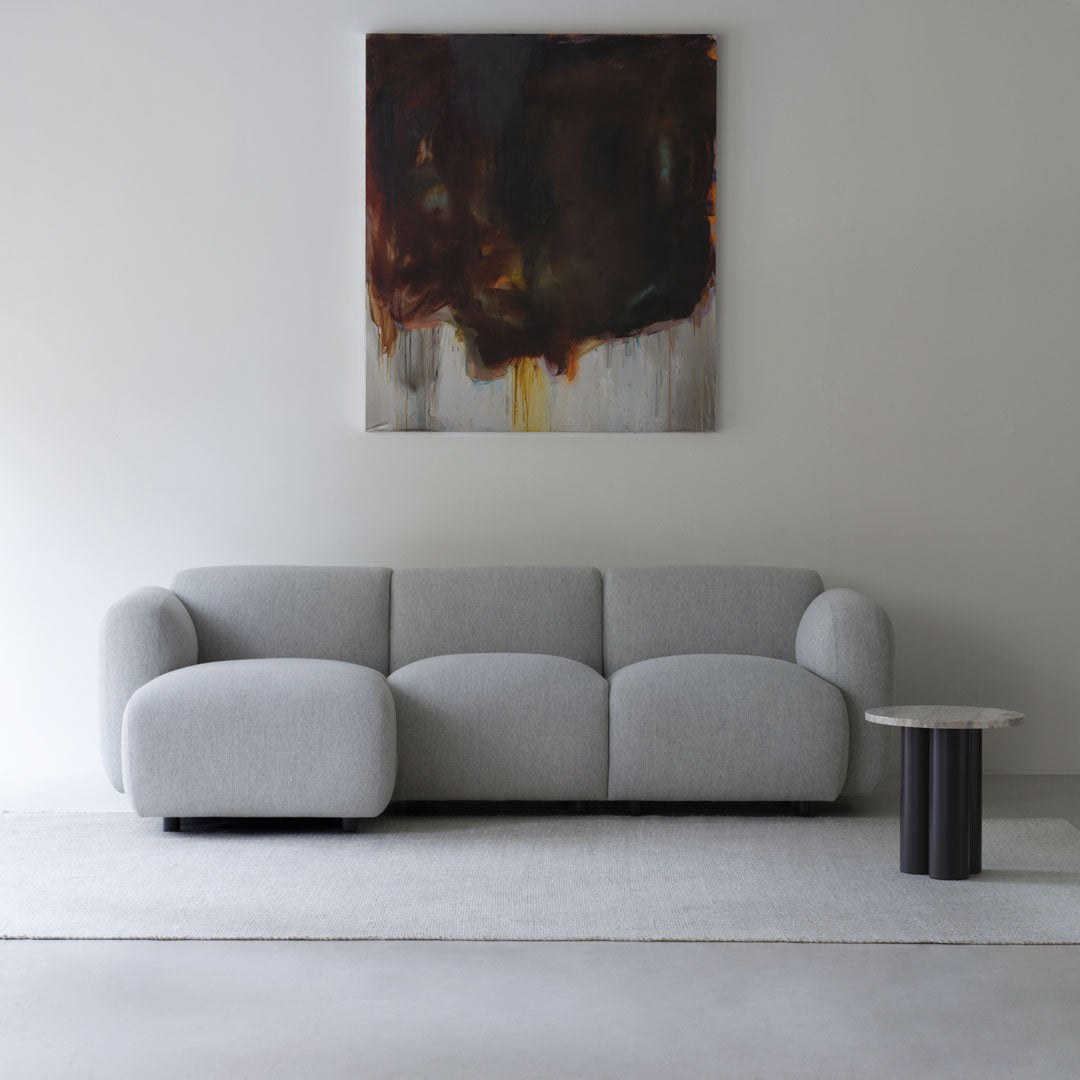 Light gray modern sofa with curved shapes and a subtle texture, paired with a dark abstract art piece on the wall.