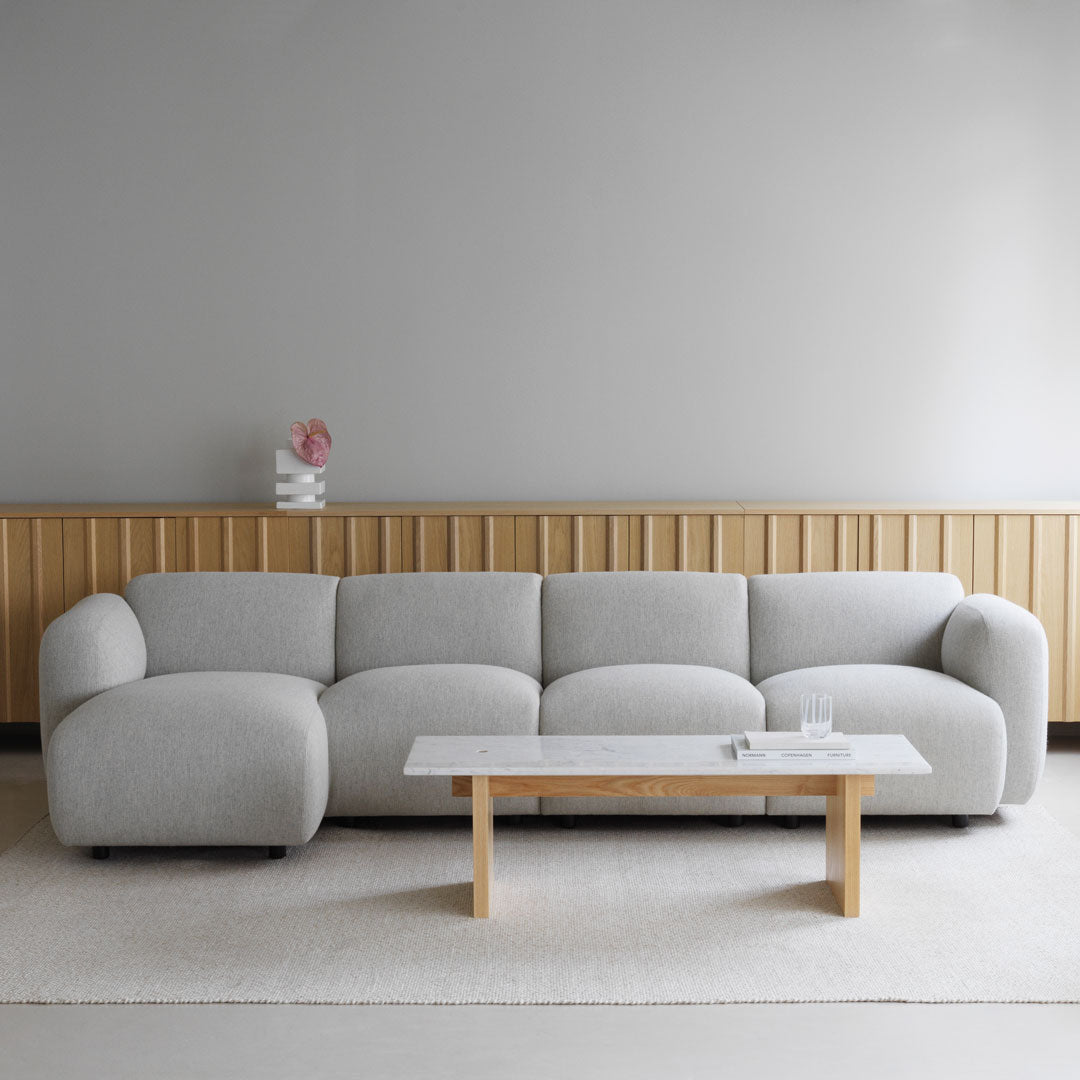 "Light gray, soft-textured sofa with rounded edges, paired with a minimalist wooden coffee table, on a neutral area rug."