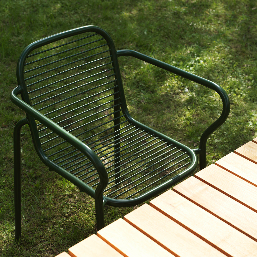 Green metal chair with a striped design, sitting beside a wooden tabletop on grassy lawn.