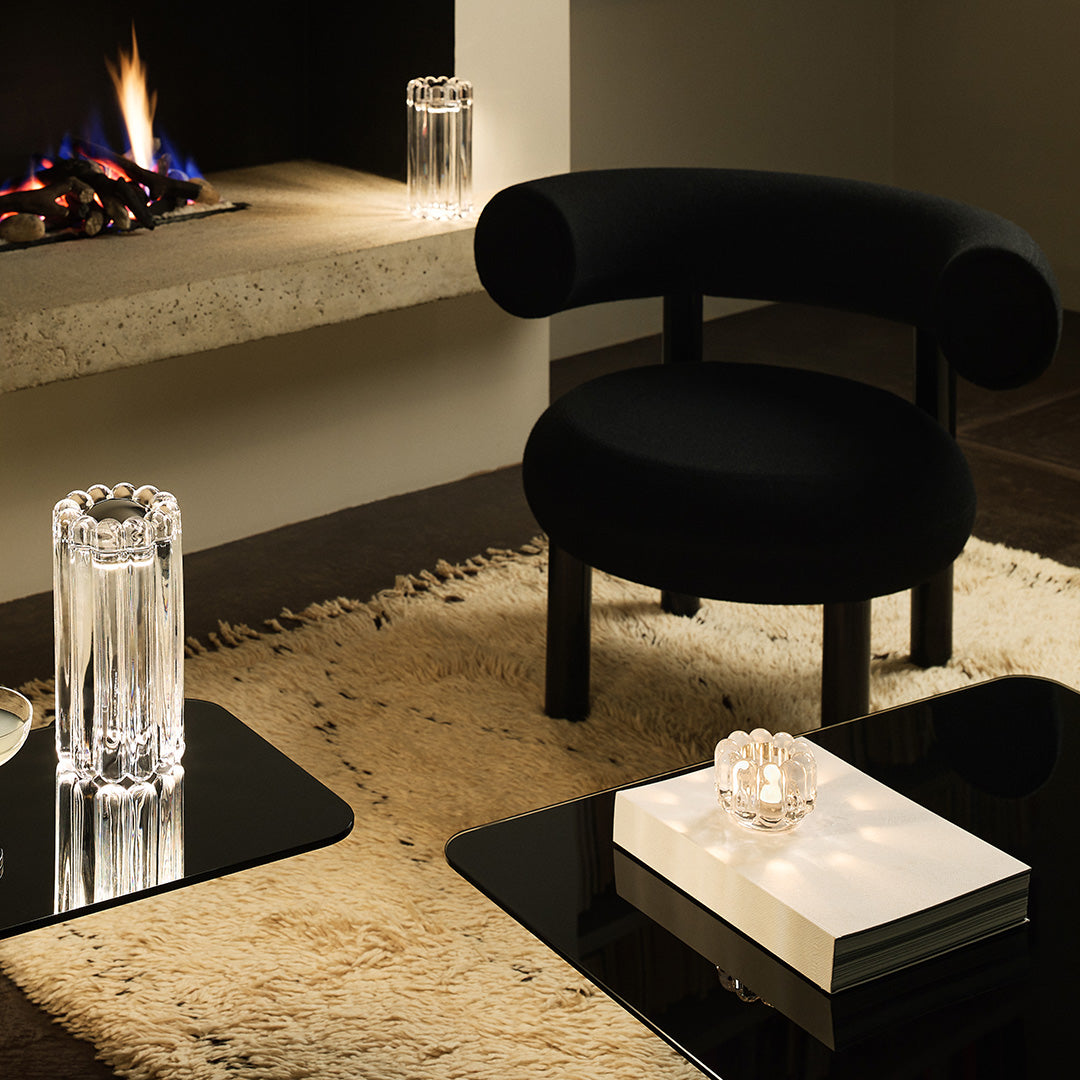 Black velvet chair sits on a beige shag rug, surrounded by clear glass accents and dark glossy tables.