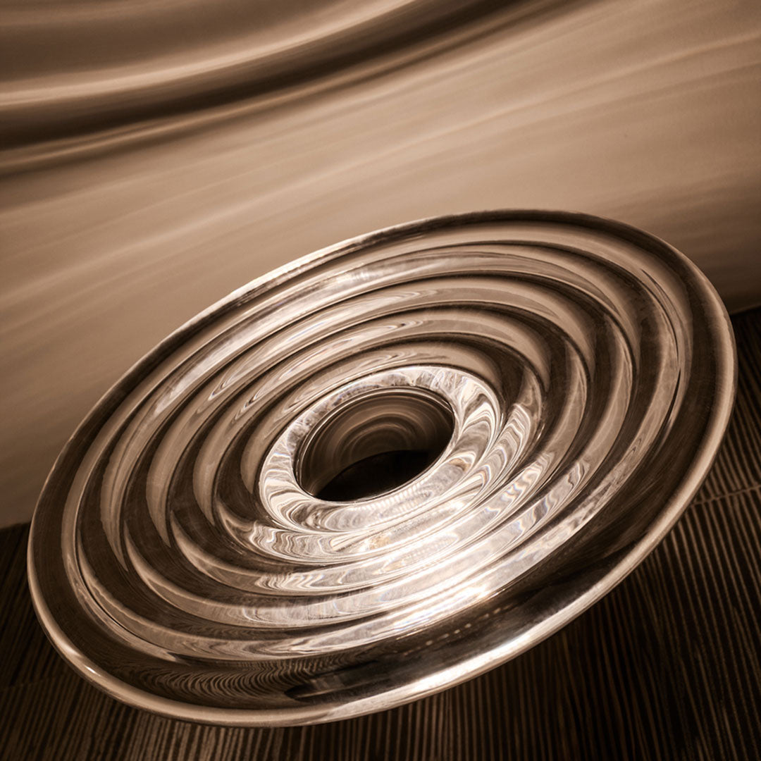 Silver circular plate with concentric ripples and a glossy finish, set against a smooth neutral background.