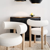 White upholstered chairs with rounded backs and wooden legs, complemented by a soft rug and dark furniture.
