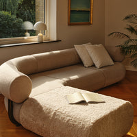 Beige curved sofa with plush texture and light-colored cushions, complemented by a warm, inviting interior setting.