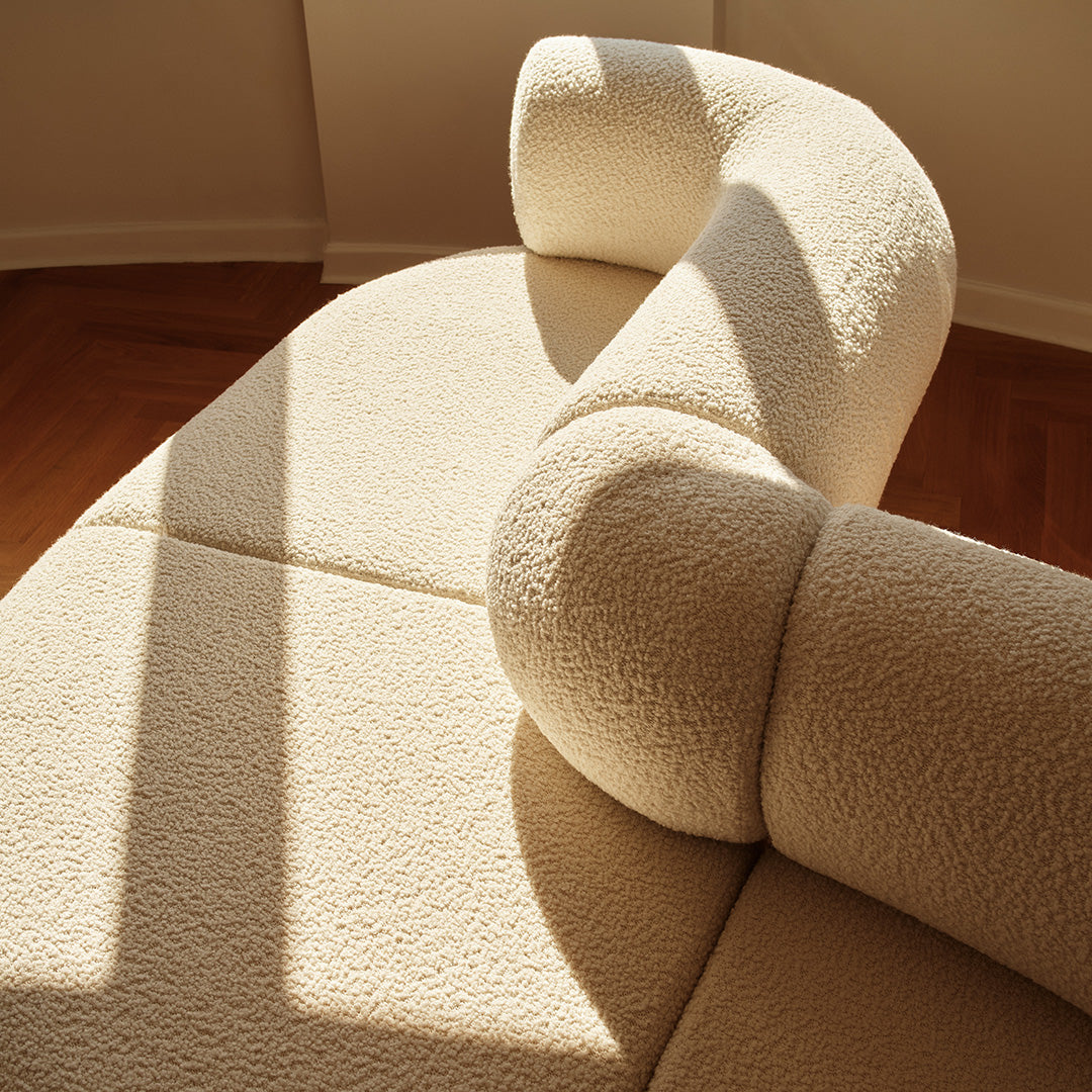 Cream-colored textured sofa with soft curves and warm light casting shadows. Elegant and cozy design.