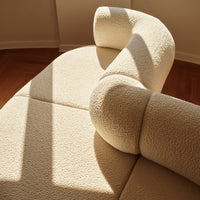 Cream-colored textured sofa with soft curves and warm light casting shadows. Elegant and cozy design.