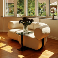 Curvy white sofa with textured fabric and sleek black glass side table, accentuated by warm wooden floor tones.