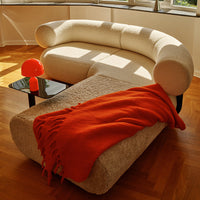 Cream curved sofa with a textured design, paired with an orange throw and matching lamp on a sleek black table.