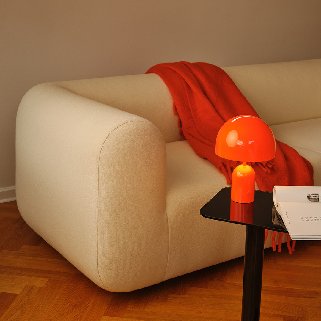 Cream-colored sofa with a vibrant orange throw blanket and a glossy orange lamp, set against warm wooden flooring.