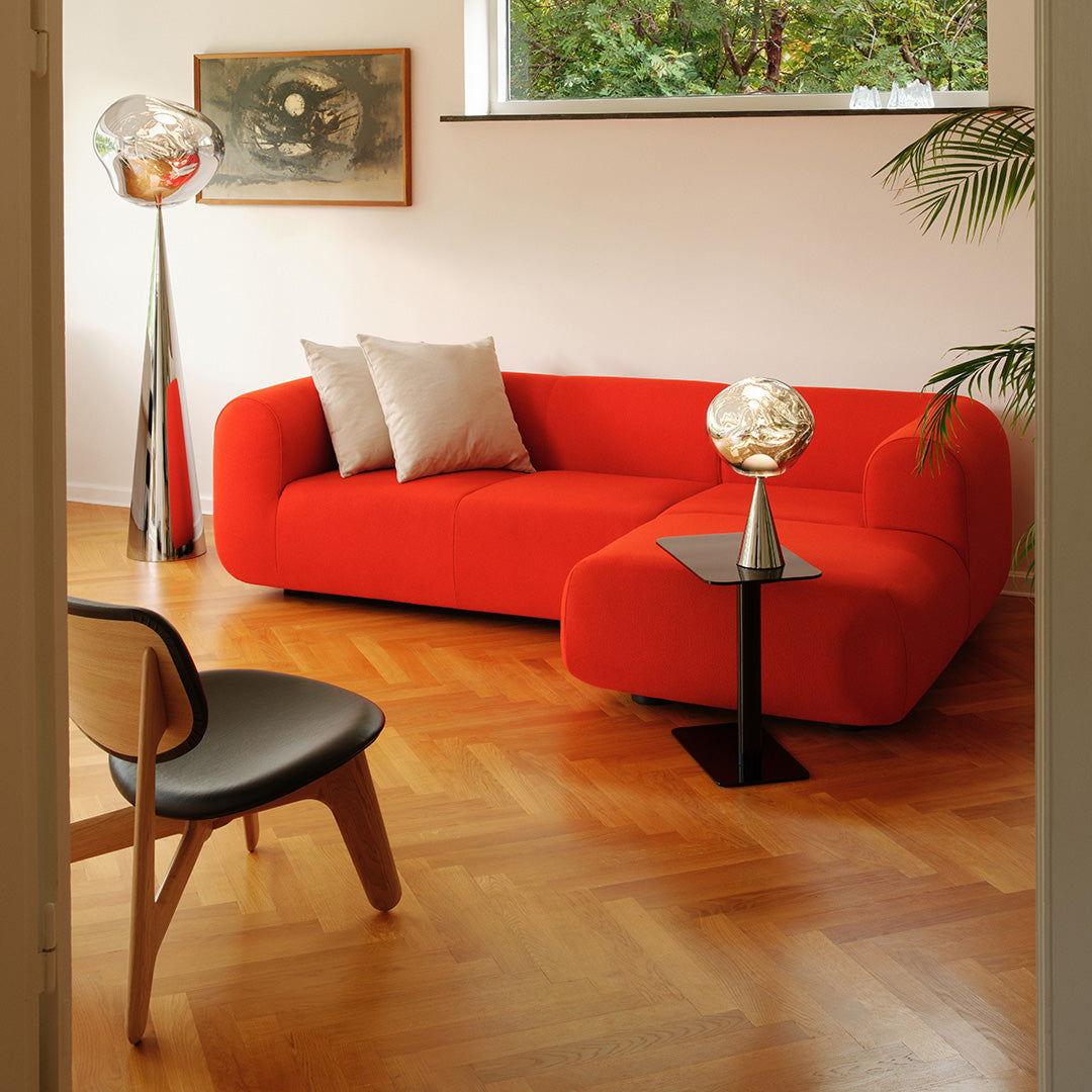 Vibrant red curved sofa with two light gray pillows, complemented by wooden flooring and sleek black accents.